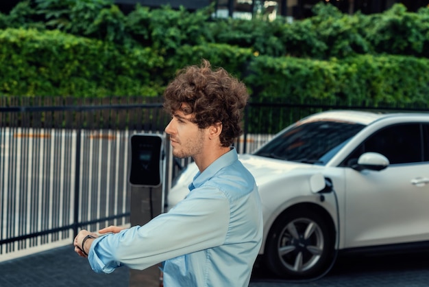 Progressive businessman with smartwatch at public charging station for EV car