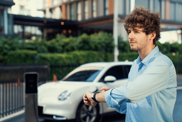 Progressive businessman with smartwatch at public charging station for EV car