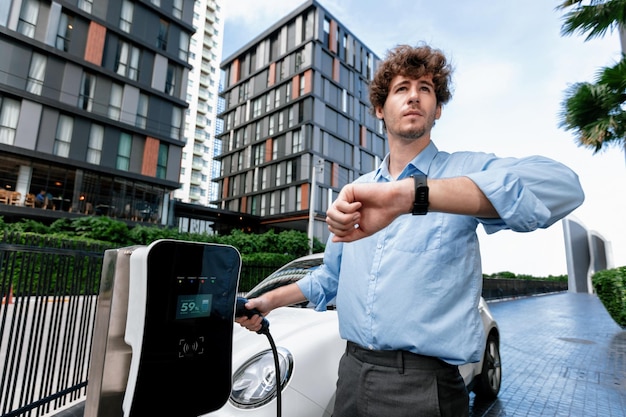 Foto uomo d'affari progressista con smartwatch presso la stazione di ricarica pubblica per auto ev