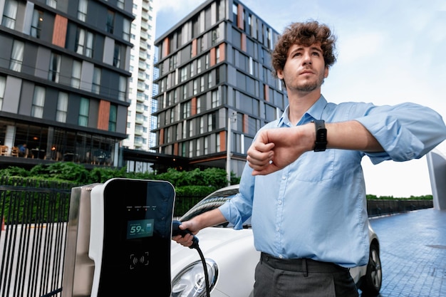 Photo progressive businessman with smartwatch at public charging station for ev car