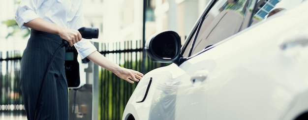 Progressive businesswoman plugs charger plug from charging station to EV