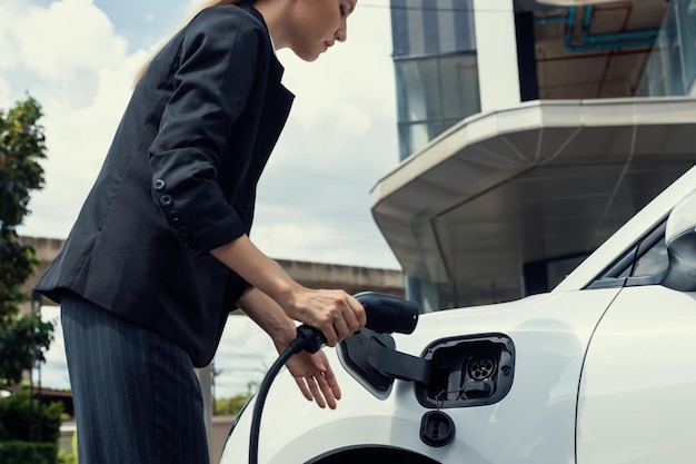 Progressive businesswoman plugs charger plug from charging station to EV