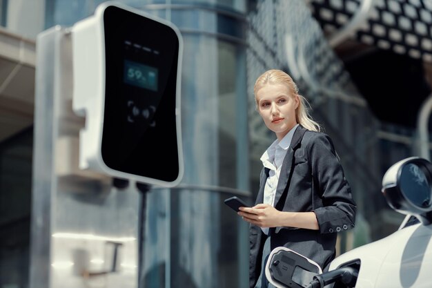 Progressive businesswoman with mockup smartphone with EV at charging station