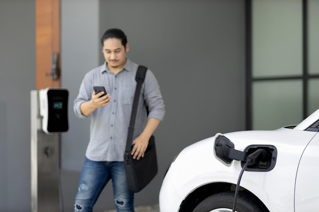 Photo progressive concept of asian man and electric car with home charging station