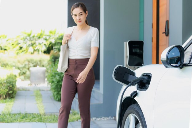 アジアの女性と家庭用充電ステーションを備えた電気自動車の進歩的なコンセプト