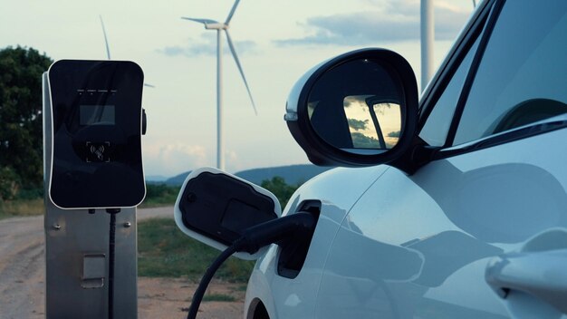 Progressive future energy infrastructure concept of electric vehicle being charged at charging station powered by green and renewable energy from a wind turbine in order to preserve the environment