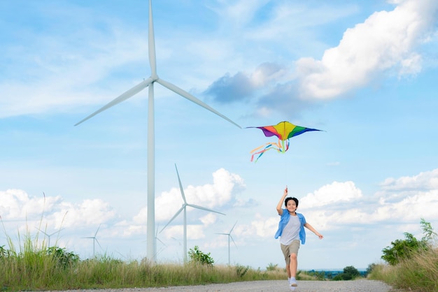写真 風力タービンの背景を持つ進歩的な幸せな少年が走り、凧を揚げる