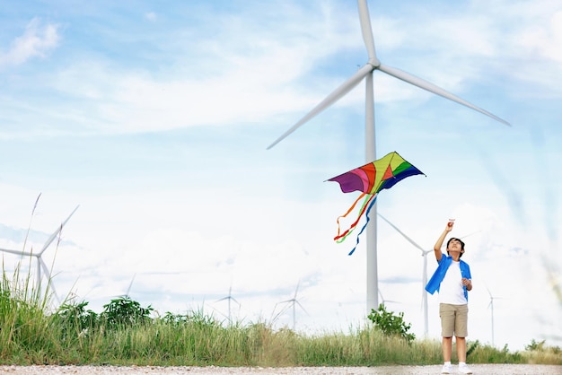 Progressive happy boy running and flying kite with wind turbine background