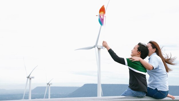 Photo progressive happy mother and her son at the wind turbine farm electric generator from wind by wind turbine generator on the country side with hill and mountain on the horizon