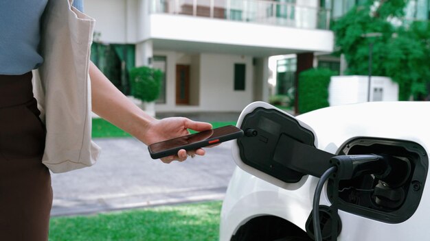 自宅で充電する電気自動車で仕事から帰ったばかりの現代女性の先進的なライフスタイル 持続可能なクリーンエネルギーを燃料とする電気自動車