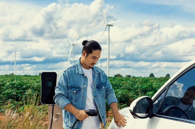 Фото Прогрессивный человек со своим электромобилем и ветряной турбиной как концепция возобновляемой энергии