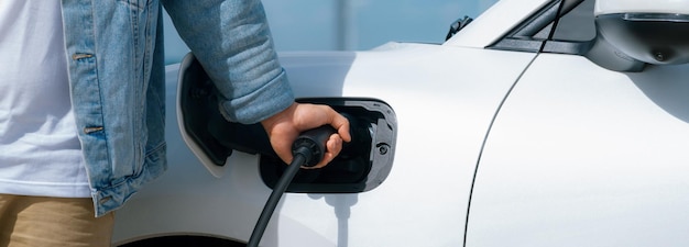 Progressive man with his ev car and wind turbine as concept of renewable energy