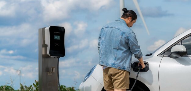 Progressive man with his EV car and wind turbine as concept of renewable energy