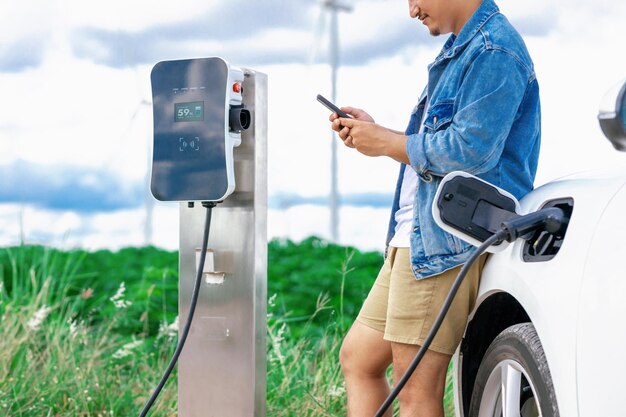 Progressive man with his EV car and wind turbine as concept of renewable energy