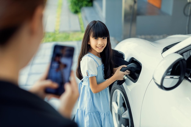 家庭でEV車を充電する娘を撮影するプログレッシブママ