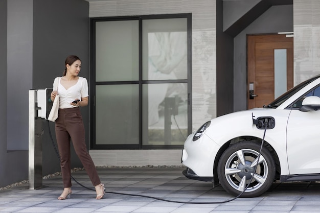 Progressive woman holding phone at EV home charging station in garage