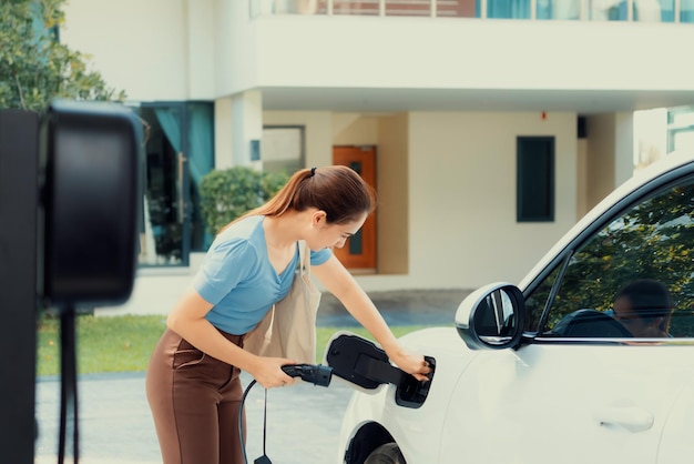 進歩的な女性が自宅の充電ステーションで EV 車を充電する