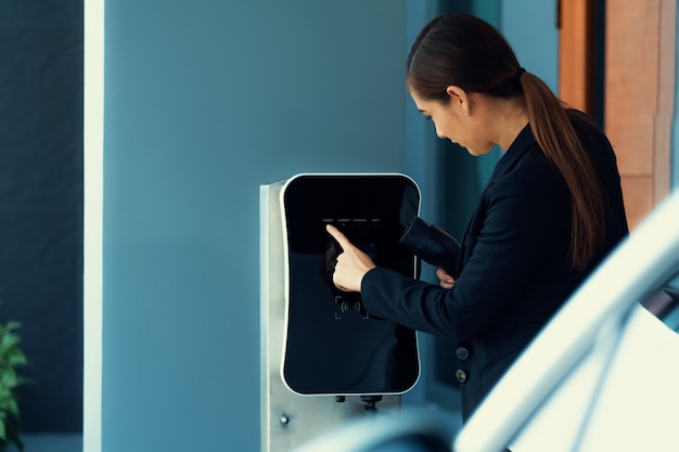 進歩的な女性が自宅の充電ステーションで EV 車を充電する