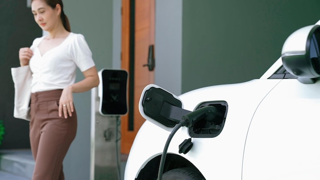 進歩的な女性が自宅で電気自動車の充電器のプラグを抜く。
