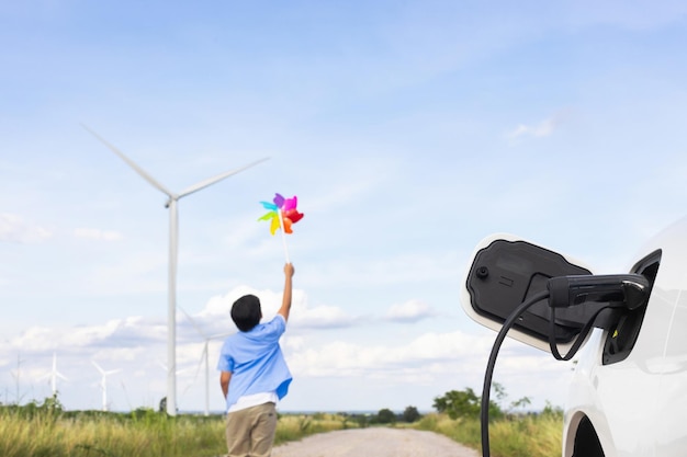 写真 風力タービン農場で風の風車のおもちゃで遊ぶ進歩的な若いアジアの少年