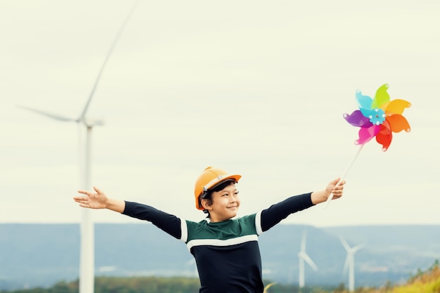 Photo progressive young asian boy playing with wind pinwheel toy at wind turbine farm