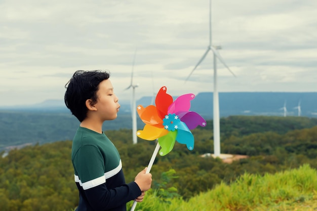 Progressive young asian boy playing with wind pinwheel toy at wind turbine farm