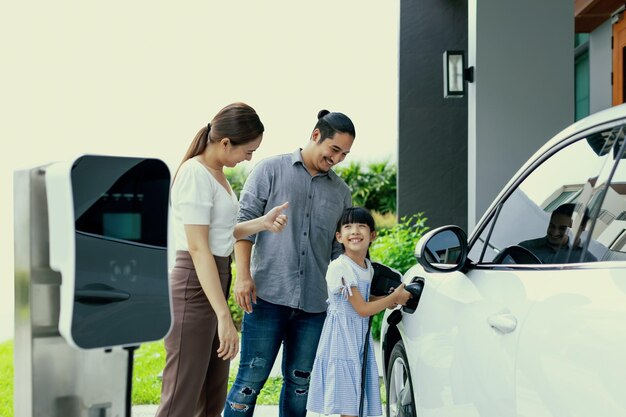 電気自動車のある家に住む進歩的な若い両親と娘