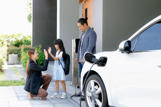 電気自動車のある家に住む進歩的な若い両親と娘