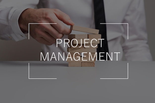 Project management text over businessman building a tower of wooden pegs