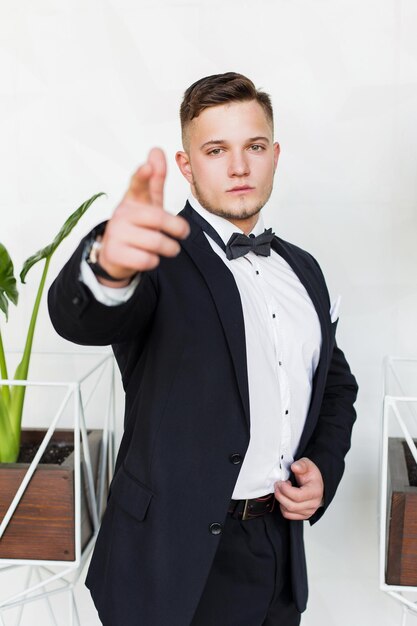 Promising young man pointing at you the next generation of businessman standing near a green plant on a white background