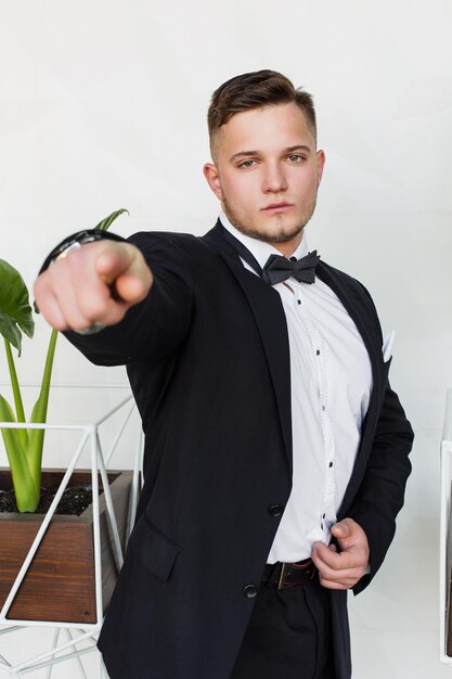 Promising young man pointing at you the next generation of\
businessman standing near a green plant on a white background