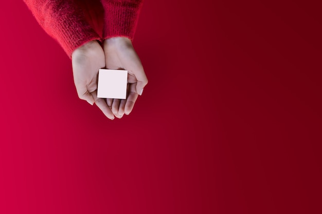 Промо-шаблон новогодней открытки Женские руки с настраиваемым пустым пространством на красном фоне