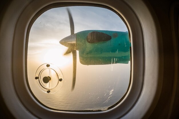 Photo propeller over sea seen through airplane window during sunset