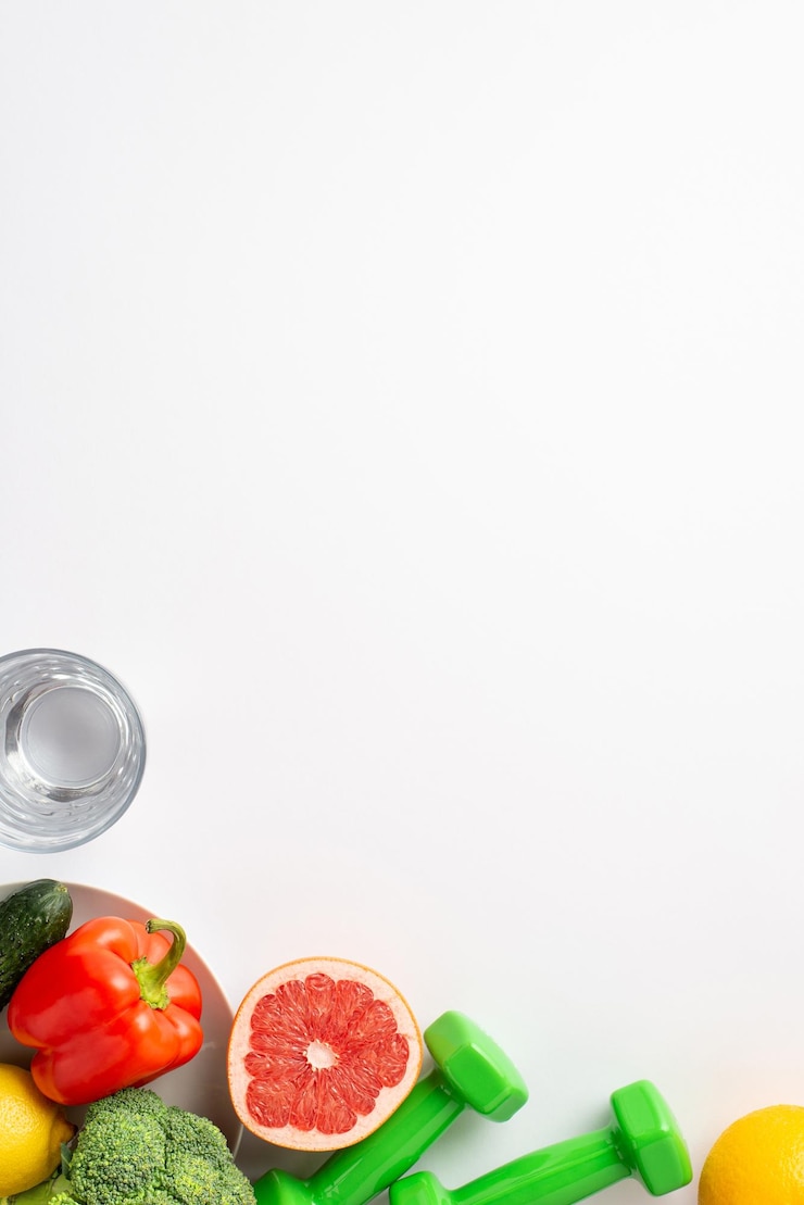 Photo proper nutrition concept top view vertical photo of plate with vegetables fruits bell pepper cauliflower cucumber grapefruit glass of water and dumbbells on isolated white background with copyspace