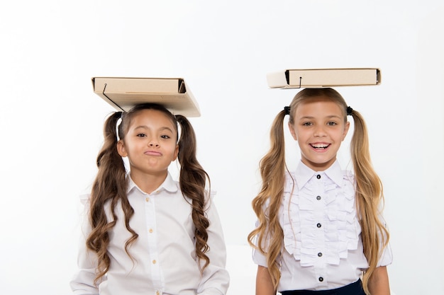 Postura corretta. studentesse con una graziosa acconciatura a coda di cavallo portano cartelle sulla testa. studentesse perfette con capelli in ordine e una postura corretta portano cartelle sulla testa. equilibrio e peso della conoscenza.