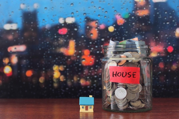 Инвестиции в недвижимость экономят деньги на концепцию дома Стеклянная банка, полная монет и миниатюрный дом
