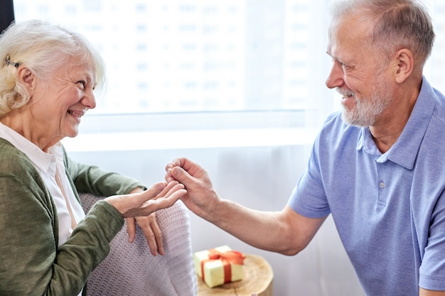 Proposal. senior man making a proposal and a happy woman smiling, grey-bearded man give golden ring to wife, at home