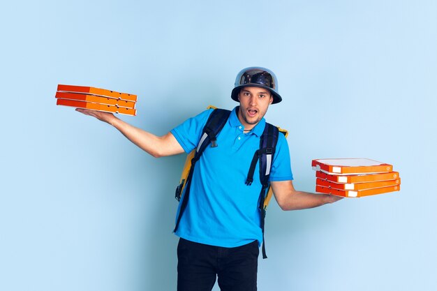 Proposing pizza. Emotions of caucasian deliveryman isolated on blue wall