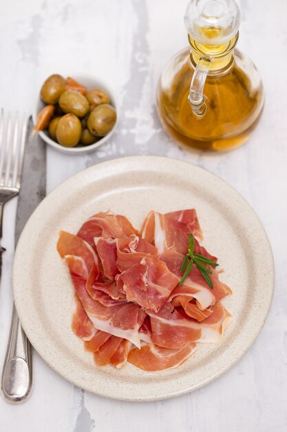 Prosciutto on dish with olive oil and olives