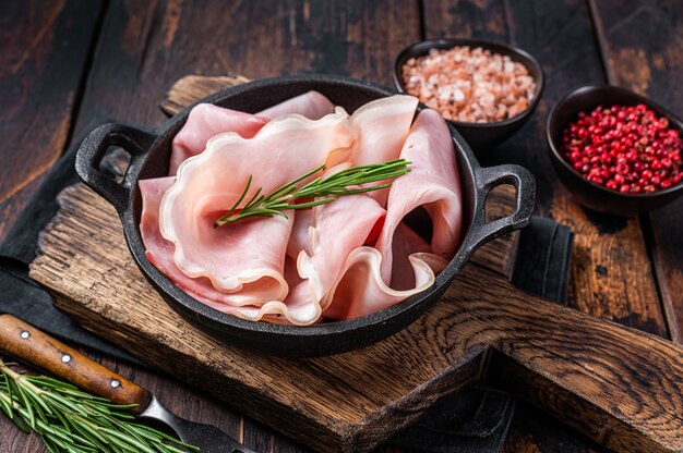 Prosciutto ham sliced in a pan. Dark wooden background. Top view.