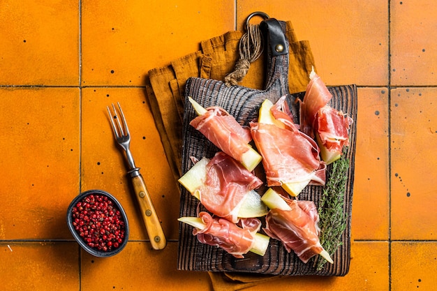 Prosciutto ham with slices of melon and fresh thyme orange background top view