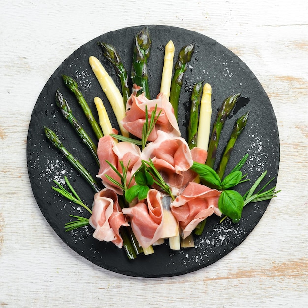 Prosciutto met gekookte asperges en kruiden op een zwarte stenen plaat Bovenaanzicht Vrije ruimte voor uw tekst