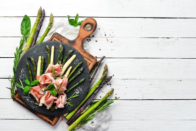 Prosciutto met gekookte asperges en kruiden op een zwarte stenen plaat. Bovenaanzicht. Vrije ruimte voor uw tekst.