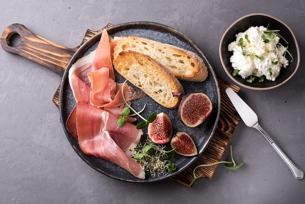 Prosciutto met sneetjes brood en vijgen op een bord op een betonnen ondergrond, Italiaanse antipasto met roomkaas, close-up.