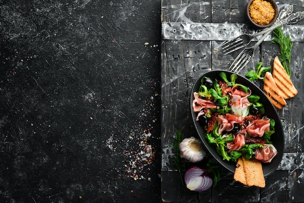 Prosciutto salad with olives in a black bowl Spanish cuisine Top view Free space for your text Rustic style