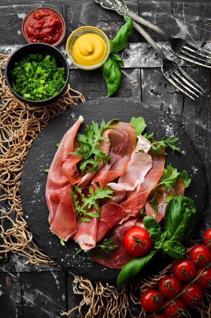 Prosciutto with arugula and basil on a black plate Spanish cuisine Top view Free space for your text