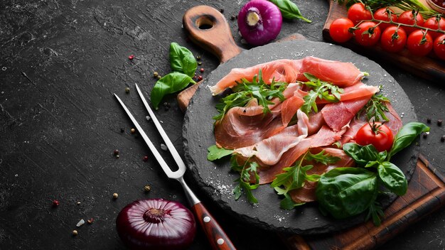 Prosciutto with arugula and basil on a black plate Spanish cuisine Top view Free space for your text