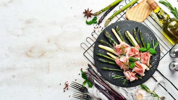 Prosciutto with boiled asparagus and spices on a black stone plate Top view Free space for your text