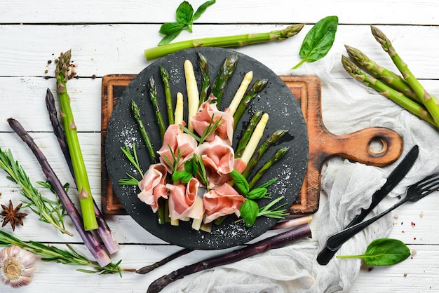 Prosciutto with boiled asparagus and spices on a black stone plate Top view Free space for your text