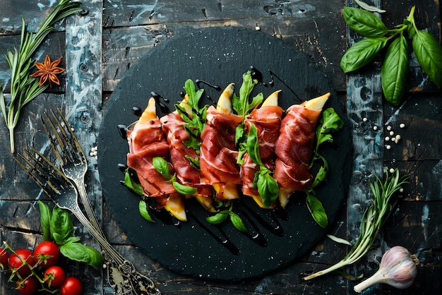 Prosciutto with pear and basil on a black stone plate Jamon Italian antipasto Top view